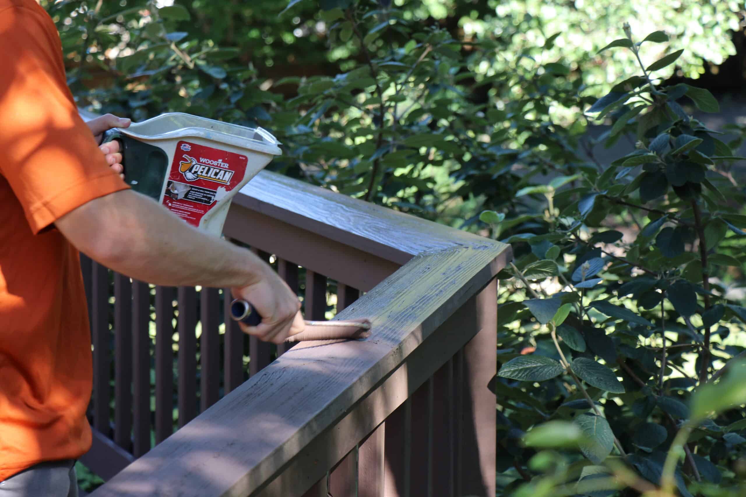 Person in an orange shirt holds a white bucket labeled Pelican on a wooden deck railing outdoors.